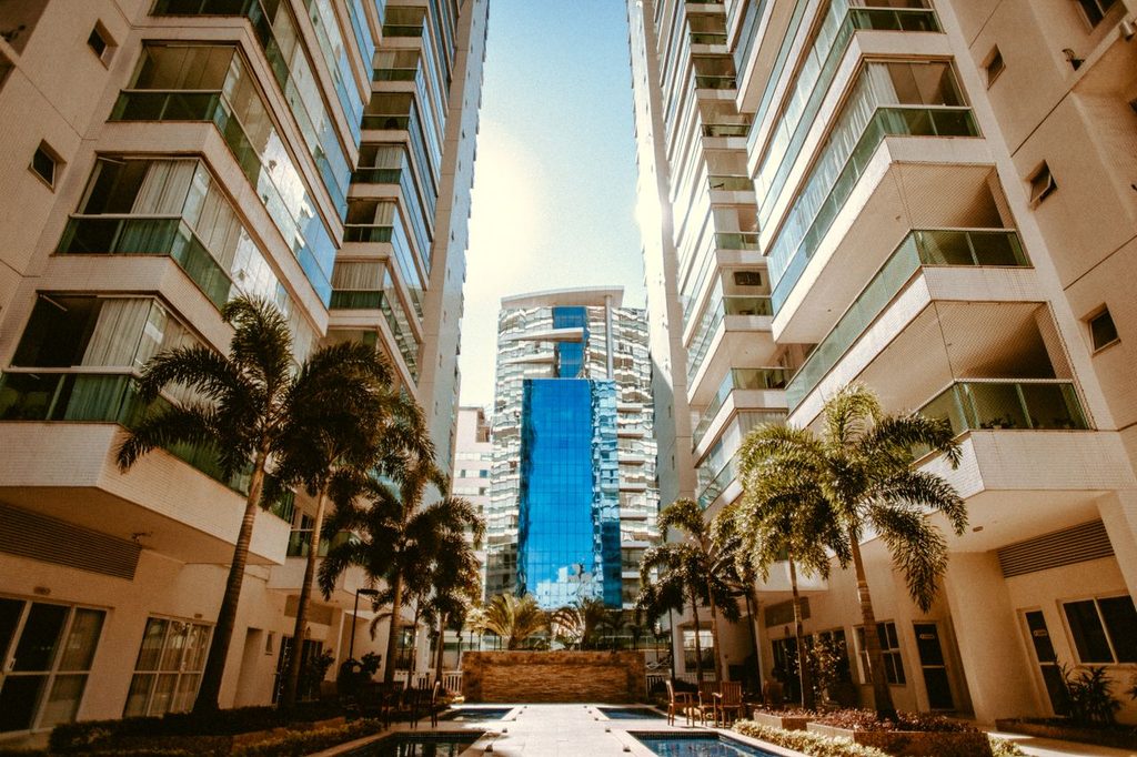 Residential towers with balconies overlooking a shared courtyard with palm trees and swimming pools