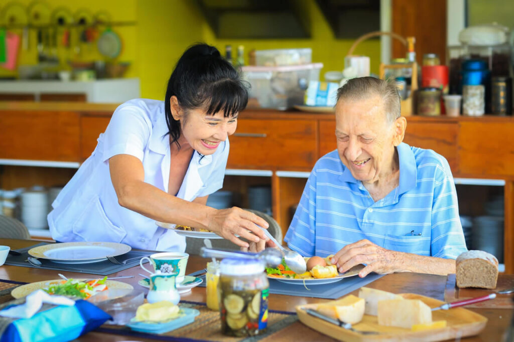 Caregiver assisting elderly resident with meal in Thailand assisted living facility