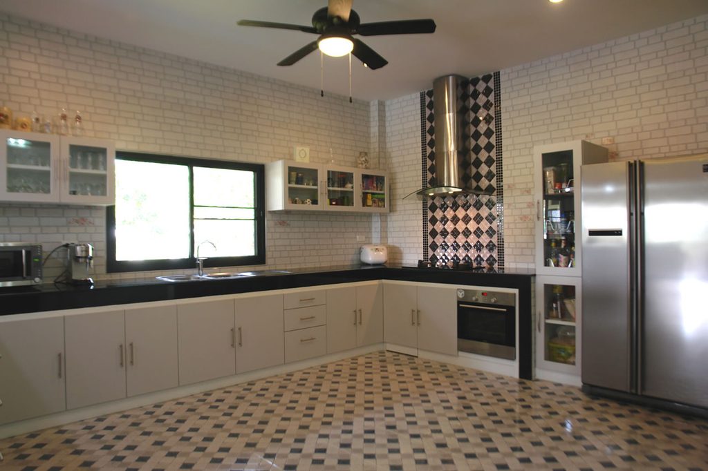 Kitchen with white cabinets, a large fridge, built-in oven, microwave, and ceiling fan