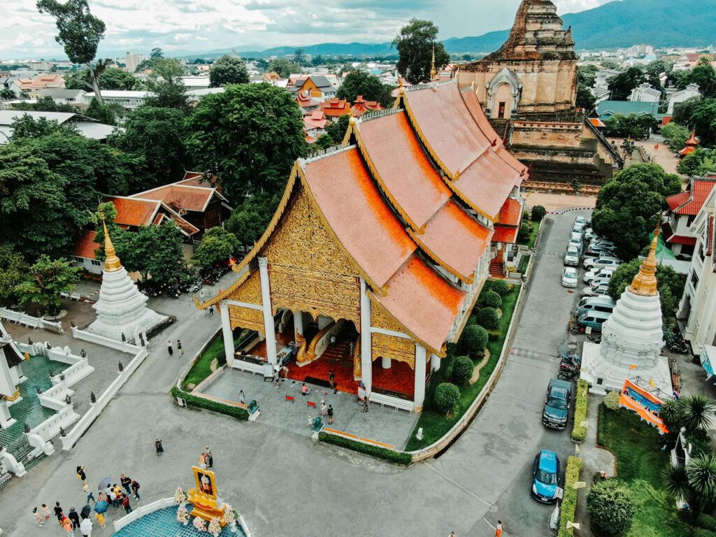 Aerial view of Wat Chedi Luang in Chiang Mai, Thailand, featuring traditional temple architecture, ancient stupa, and surrounding cityscape with mountains in the background.