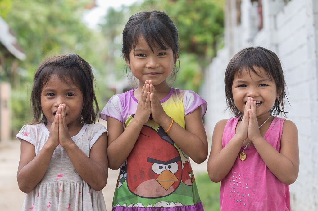 Three young children performing the traditional Thai wai greeting as a sign of respect