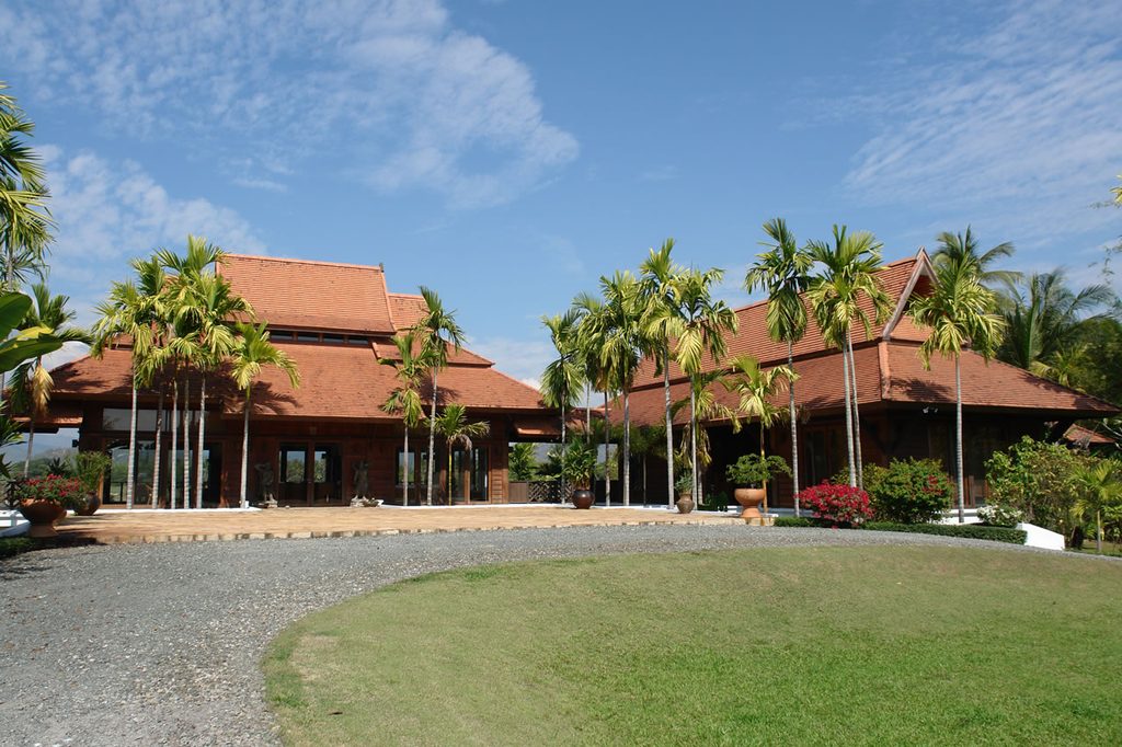 Thai-style house with terracotta tiled roofs, palm trees and a landscaped garden.