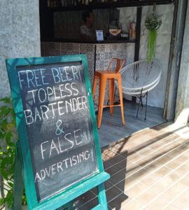 Bar sign joking about false advertising with promises of free beer and a topless bartender