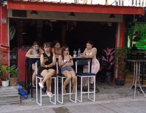 Five bar girls sitting outside, all staring at their phones