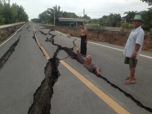 Man standing waist-deep in a giant crack splitting a rural Thai road