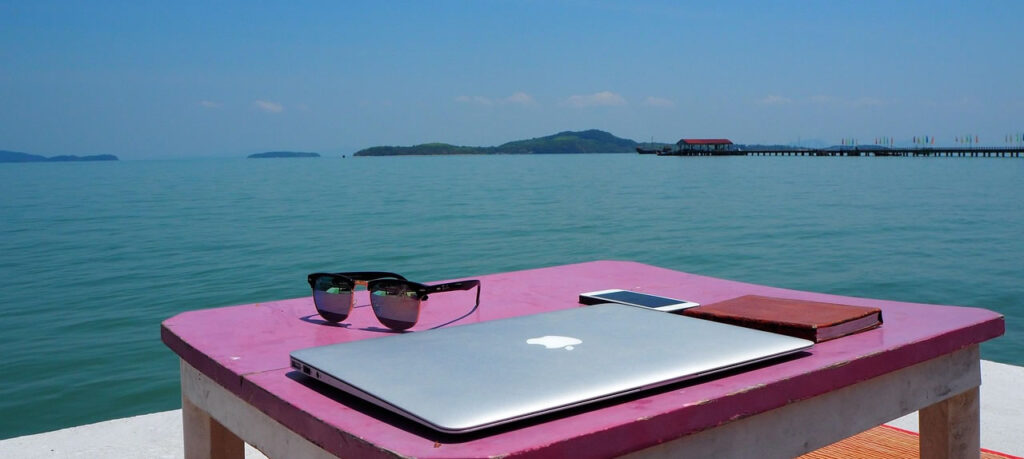 Seaside table with laptop, sunglasses, and smartphone on Koh Lanta, overlooking calm ocean and distant islands