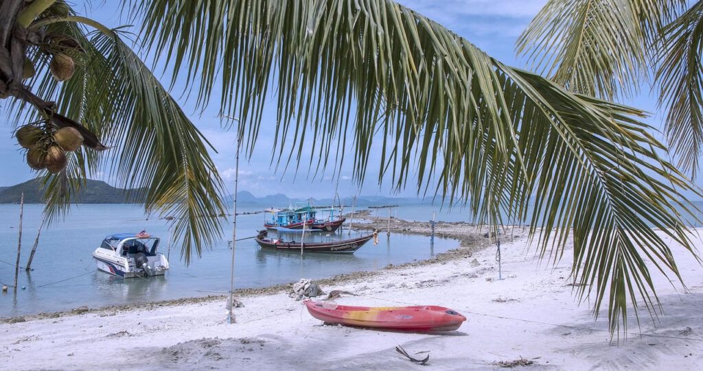 Peaceful beach in Ko Samui with palm trees, fishing boats, and kayak on white sand
