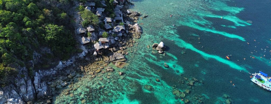 Aerial view of Koh Tao with coral reefs, snorkeling swimmers, and cliffside bungalows