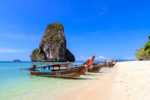 Longtail boats lined up on the shore of Railay Beach with towering limestone cliffs in Krabi, Thailand