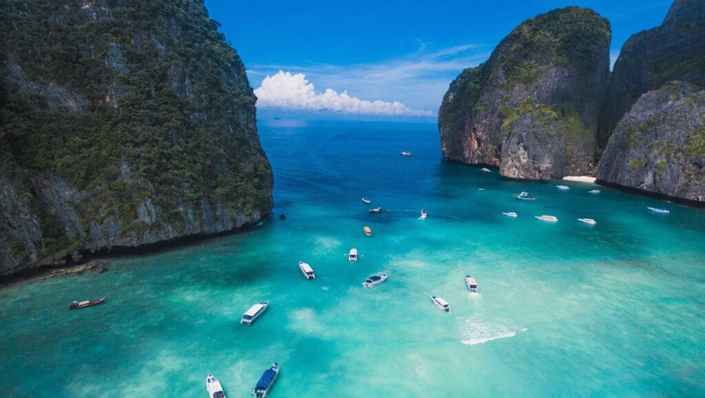 Aerial view of speedboats anchored in the turquoise waters of Maya Bay, surrounded by towering limestone cliffs on Koh Phi Phi Leh, Thailand