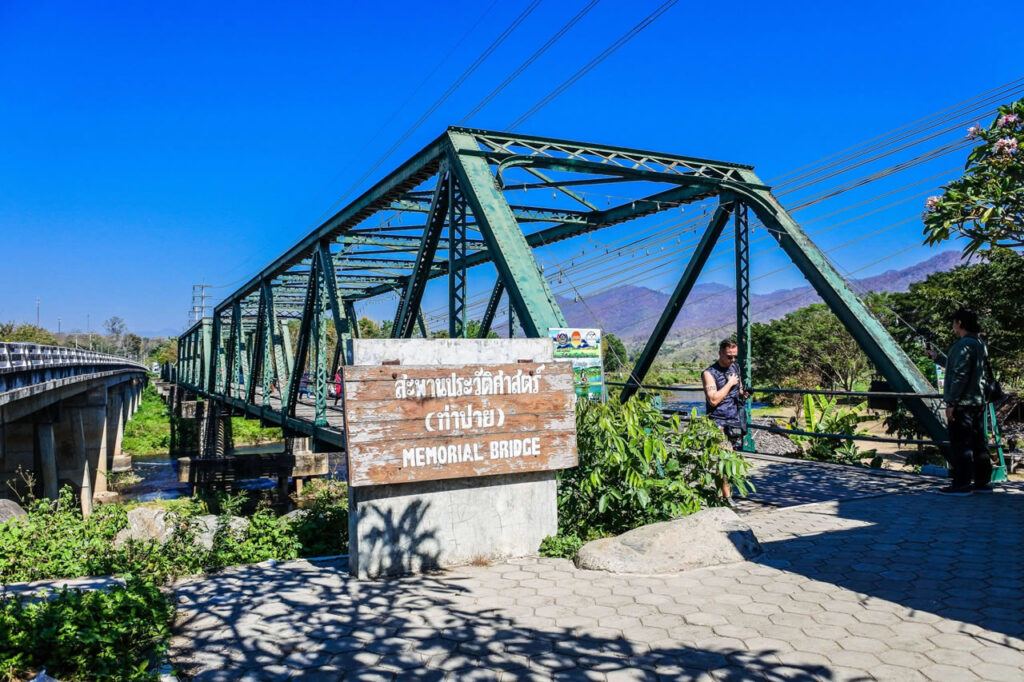 Historic Memorial Bridge in Pai, Thailand with mountain backdrop and tourist activity