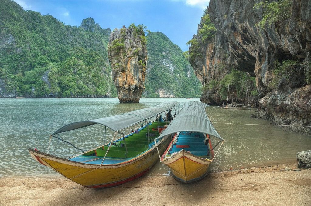 Traditional longtail boats docked near towering limestone cliffs at James Bond Island in Phang Nga Bay, Thailand
