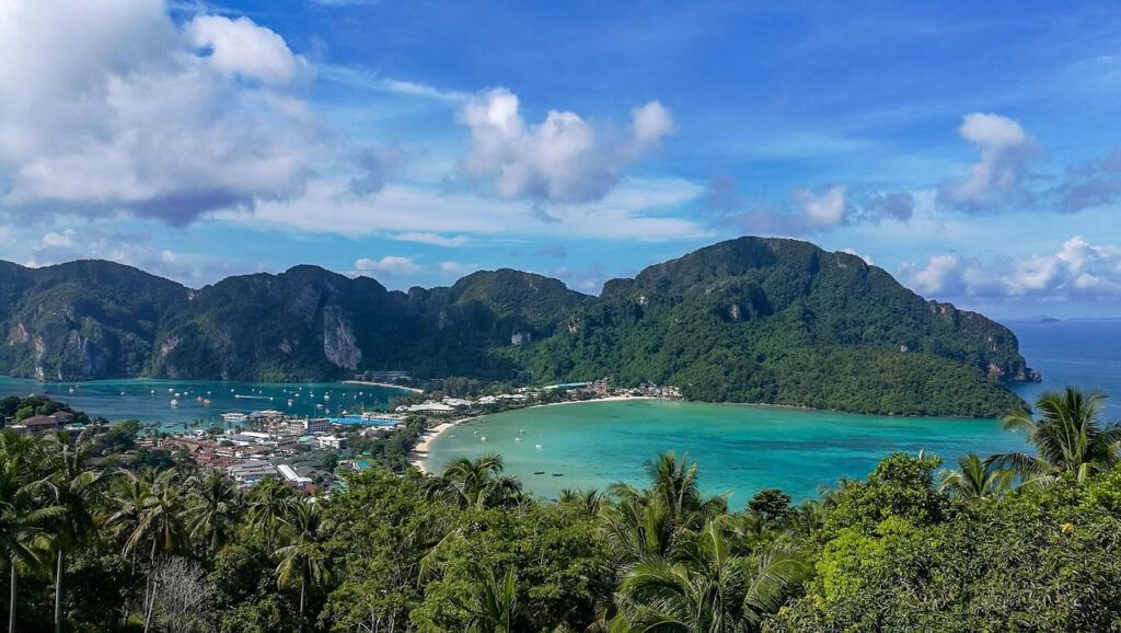 Panoramic view from the Phi Phi Viewpoint overlooking Tonsai Bay and Loh Dalum Bay with turquoise water, lush cliffs, and boats anchored along the coast