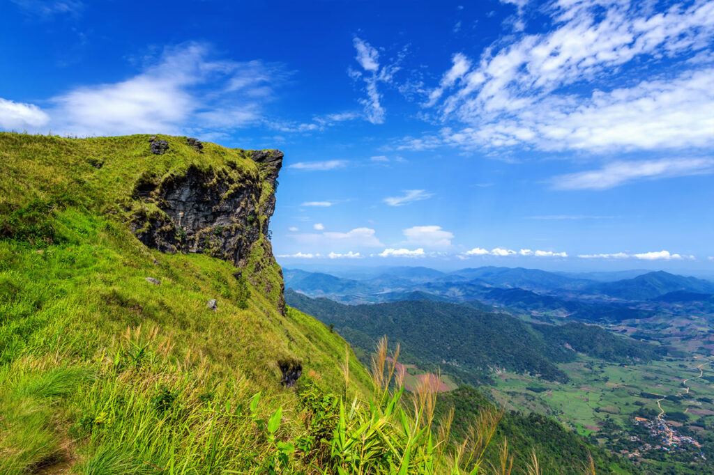 Scenic cliffside view from Phu Chi Fah overlooking forested mountains and valleys in Chiang Rai, Thailand under a bright blue sky