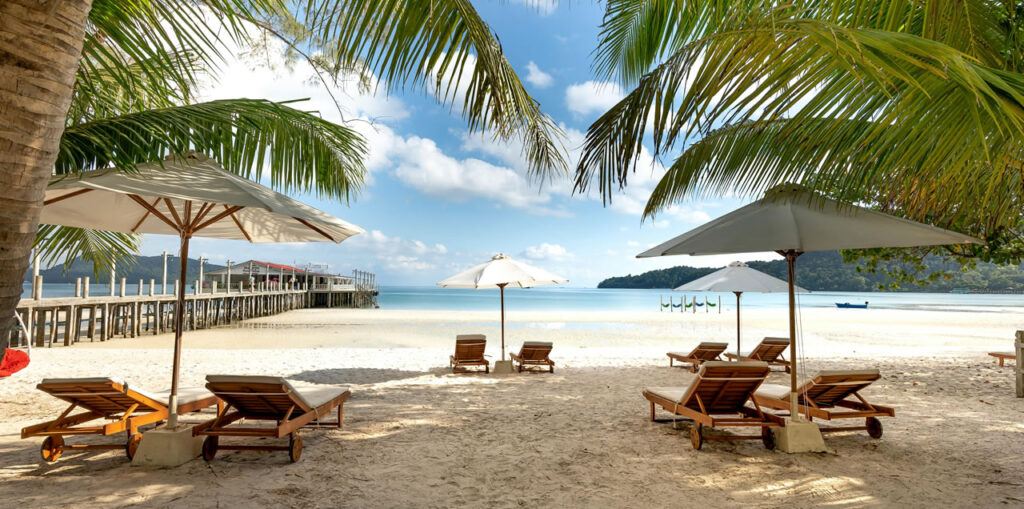 Tropical beach in Phuket with sun loungers, umbrellas, and wooden pier under palm trees