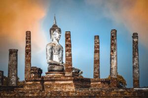 Sunset reflecting on temple ruins and Buddha statue in Sukhothai Historical Park, Thailand