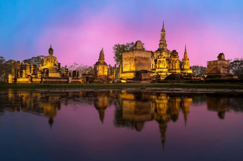 Temples of Sukhothai lit up at twilight with colorful sky and reflection in the water