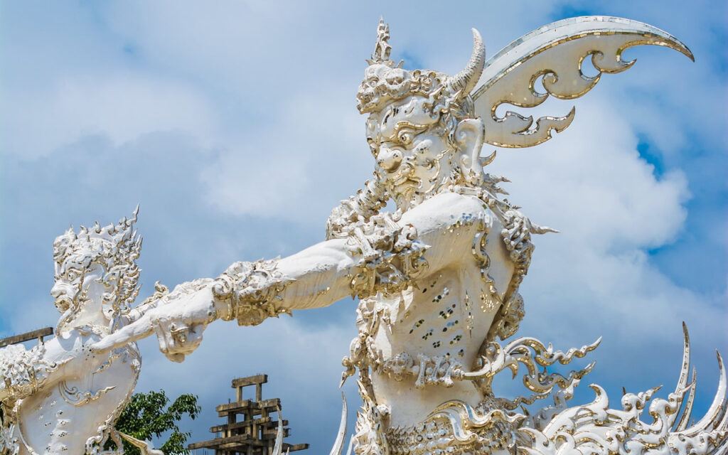 Ornate white demon guardian with wings and horns at the entrance of Wat Rong Khun