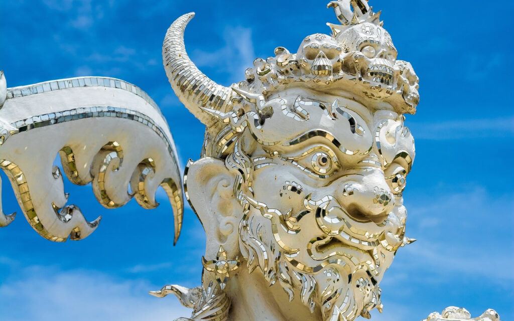 Close-up of fierce guardian demon statue with mirrored details at Wat Rong Khun