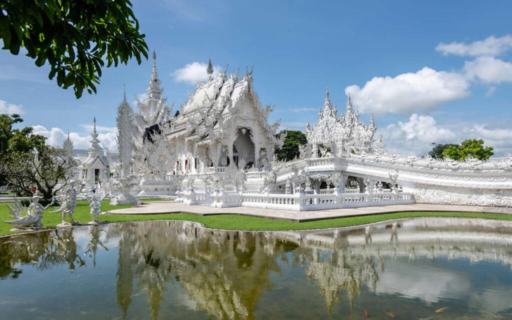 Wat Rong Khun (White Temple) reflected in pond under a blue sky in Chiang Rai