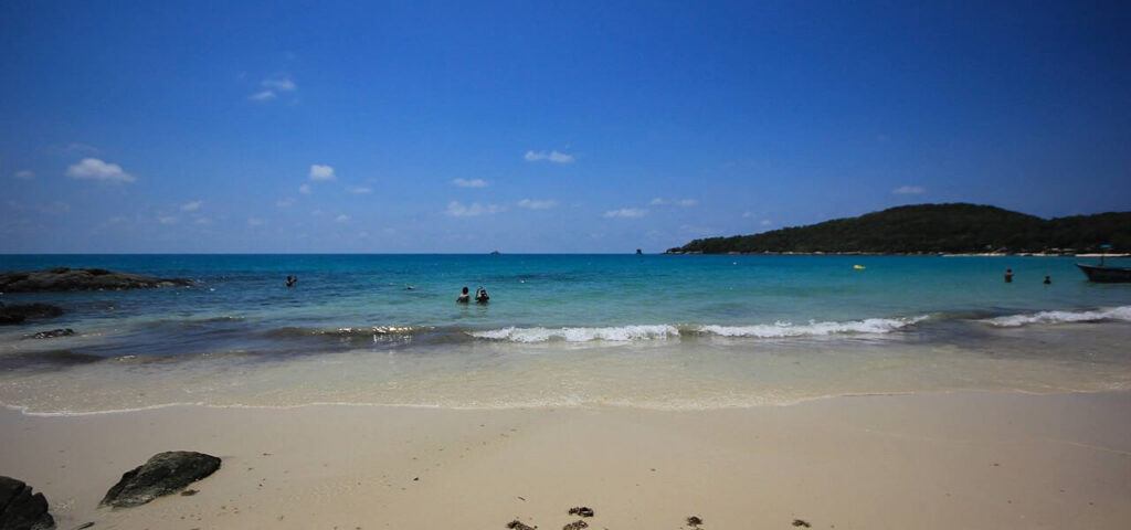 View of a quiet beach on Koh Samet, with turquoise water, white sand, and a lush green headland under a clear blue