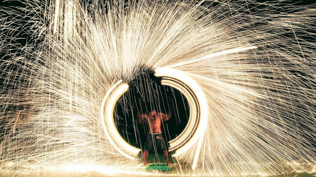 Fire show performer creating a circle of sparks on the beach at night in Koh Samet, Thailand
