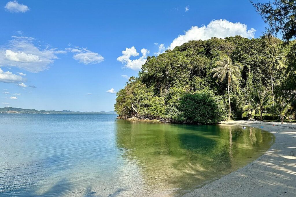 Half Moon Beach on Koh Chang with clear turquoise water, white sand, and lush green trees under a bright blue sky