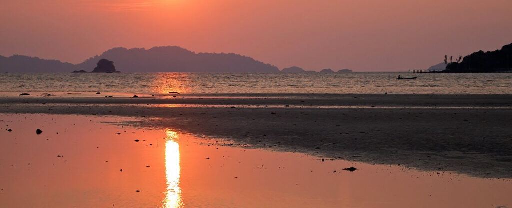 Fiery sunset over the beach on Koh Mak, Thailand, with calm waters reflecting the red-orange sky and silhouettes of distant islands