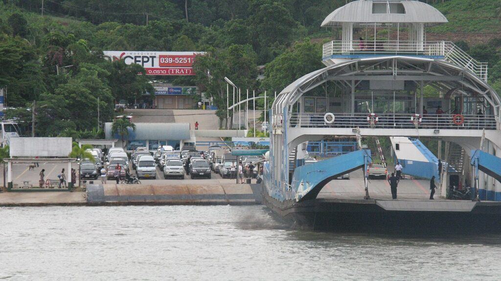 Car ferry docked at Koh Chang pier with vehicles boarding and lush green hills in the background