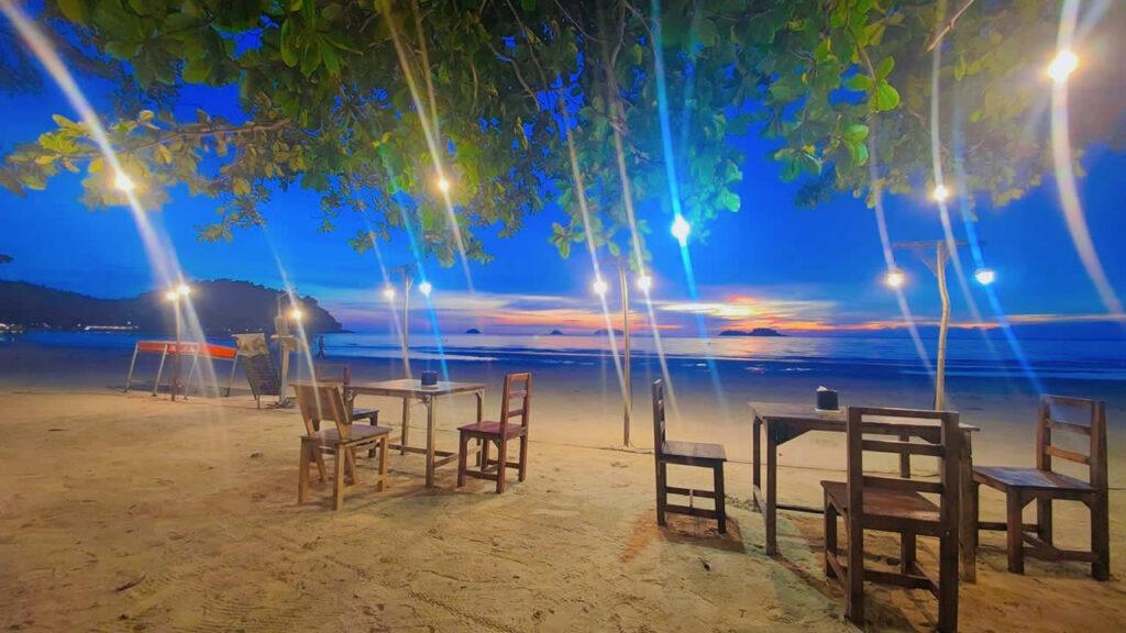 Beachfront dining at Lin’s Bungalow on Koh Chang at sunset with tables on the sand