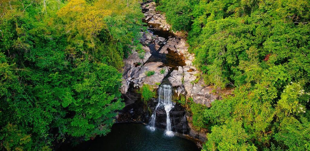 Aerial view of Khlong Chao Waterfall on Koh Kood, Thailand, surrounded by lush green jungle and rocky cliffs with a natural pool below.