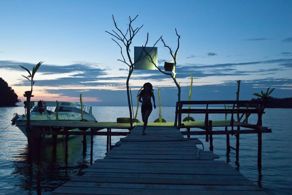 Twilight view at Bang Bao Pier, Koh Kood, Thailand, with a silhouette of a girl walking, a moored boat, and the sky glowing in soft evening colors.