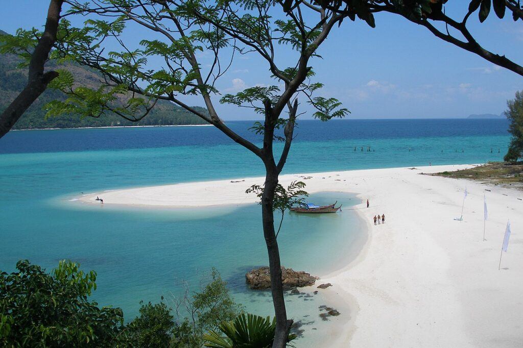 White sand beach and turquoise water on Koh Lipe, Thailand, with longtail boat and tourists walking along the shore