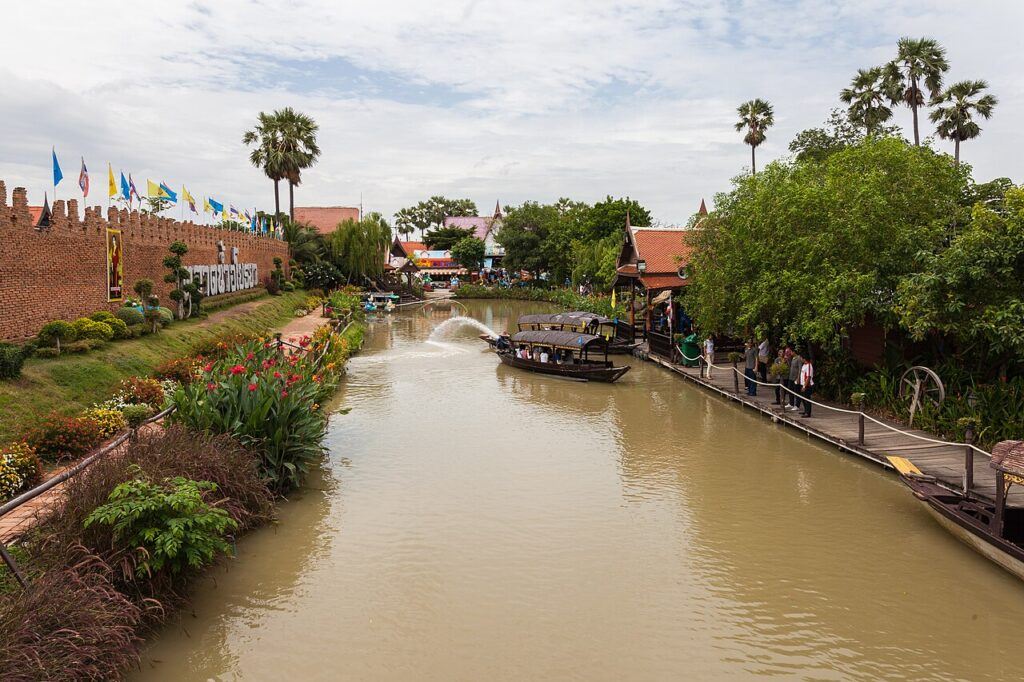 Traditional wooden boats at the Ayutthaya Floating Market in Thailand, with shops, walkways, and canalside greenery.