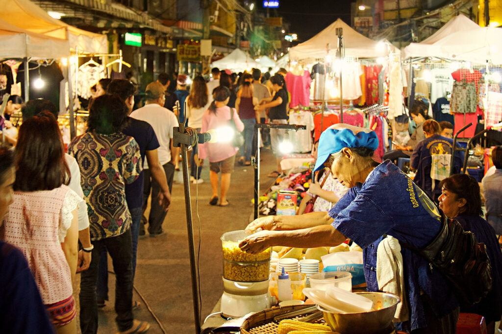 Vendor preparing food at Chiang Rai Night Bazaar, with crowds browsing stalls and enjoying the lively evening market atmosphere.