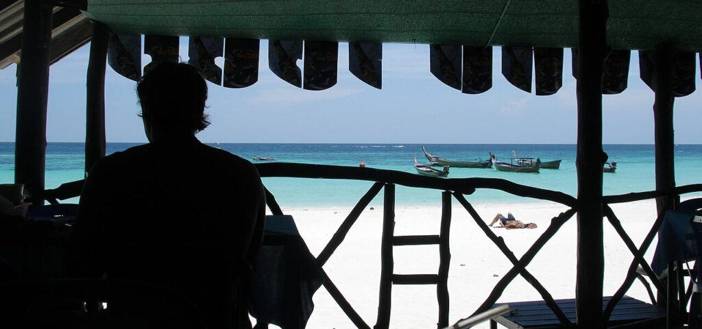 View from a beach shack on Koh Lipe with person sitting inside and longtail boats on the turquoise water