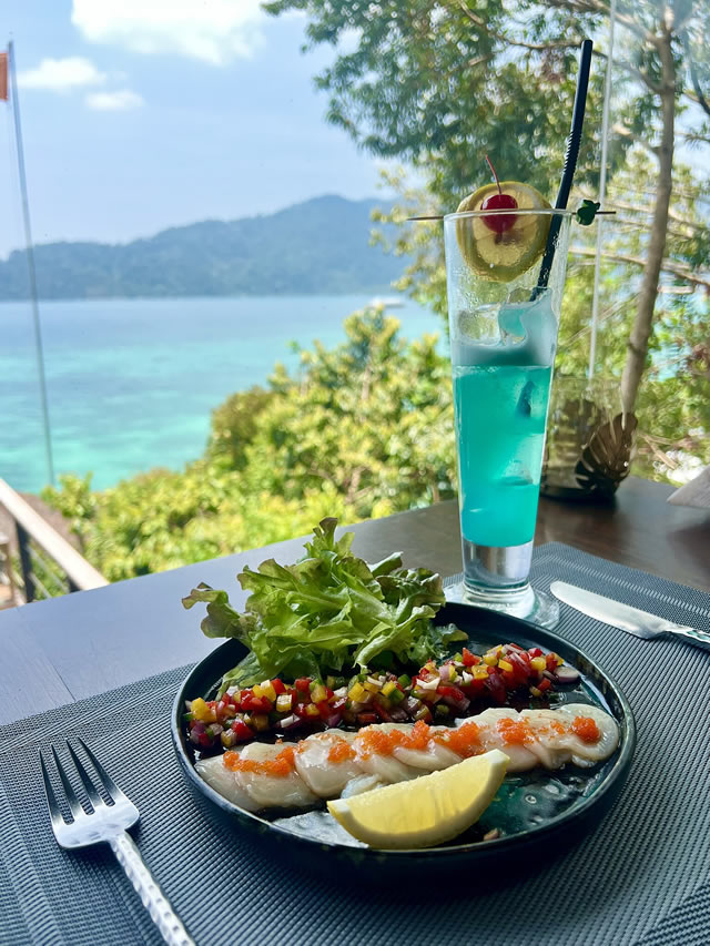 Seafood dish with salad and blue cocktail overlooking the ocean in Koh Lipe, Thailand