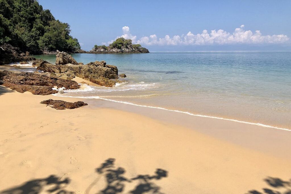 Golden sandy beach with turquoise water and rocky shoreline on Koh Phayam island, Ranong Province, Thailand.