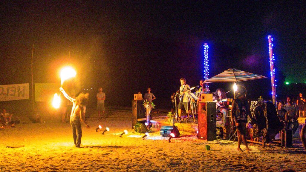 Fire dancer performing on the beach with a live band and colorful lights during a nightlife event on Koh Phayam, Thailand.
