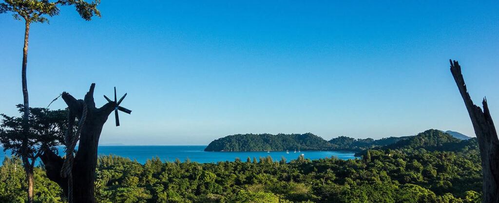 Scenic view of lush green forest and turquoise sea with islands in the distance on Koh Phayam, Thailand.