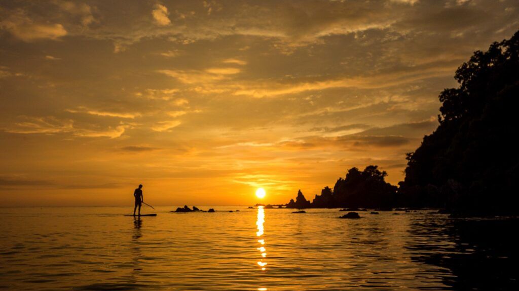 Silhouette of a person paddleboarding during a golden sunset on Koh Phayam, Thailand.
