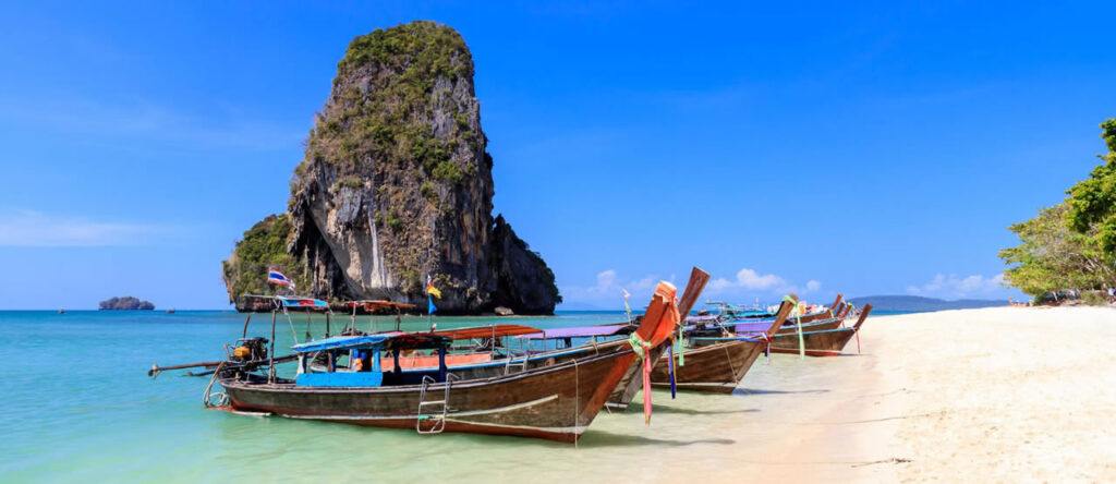Traditional longtail boats on a sandy beach with limestone cliffs in Krabi, Thailand