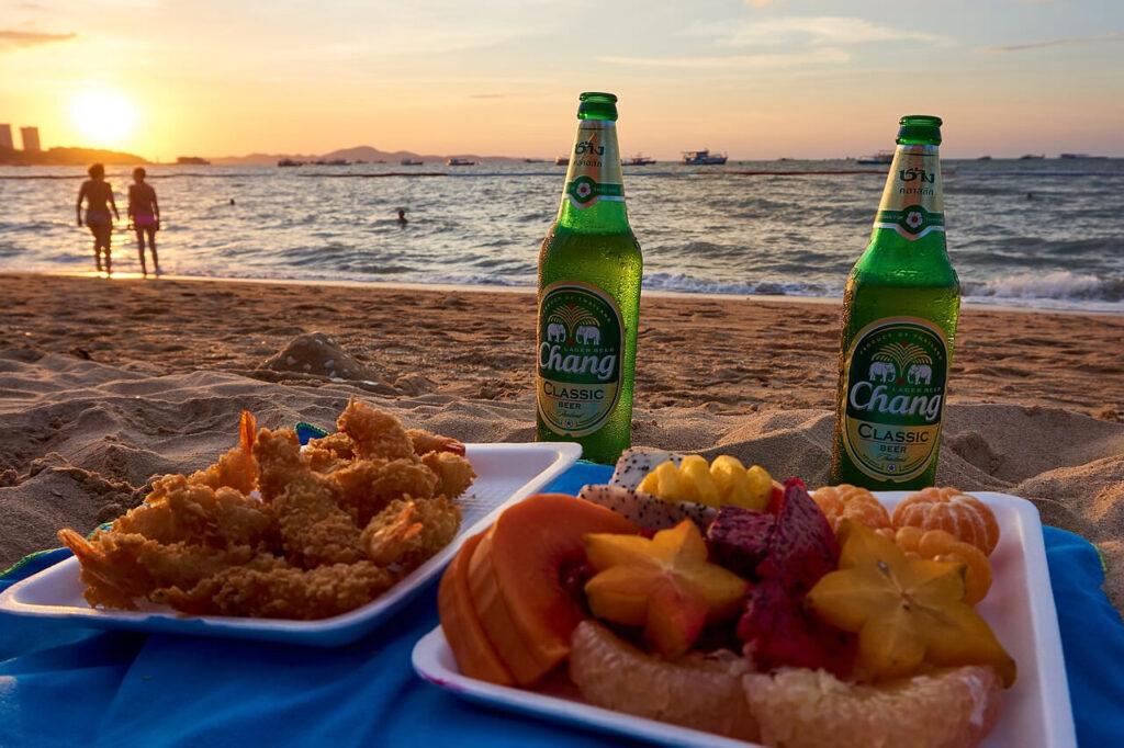 Sunset picnic on Pattaya Beach with fried shrimp, tropical fruit, and drinks.