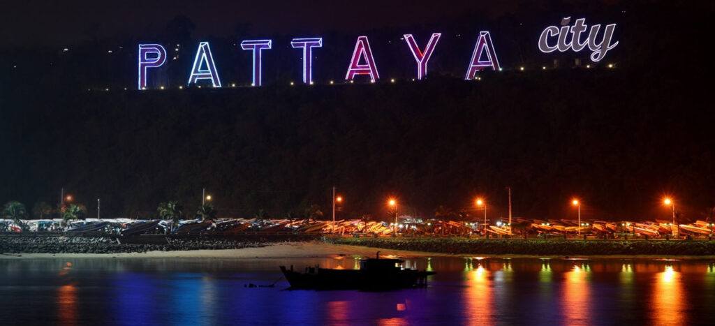 Illuminated Pattaya City sign glowing at night above the bay.