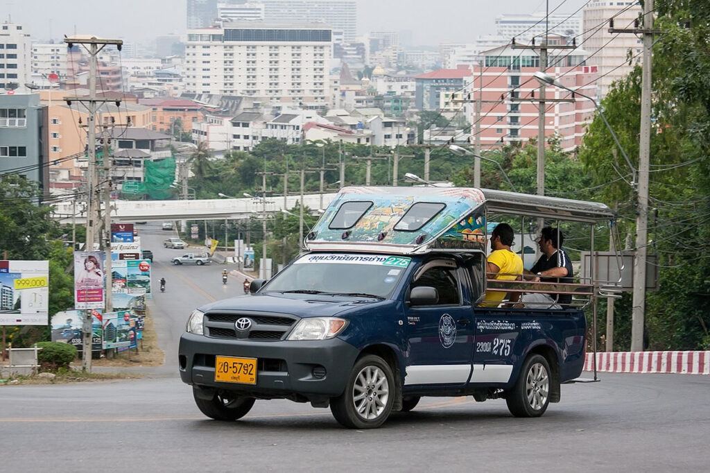 Blue songthaew shared taxi driving through Pattaya with passengers on board.