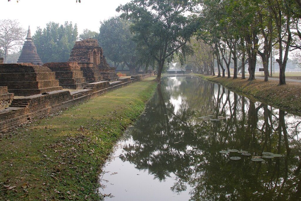 Moat and ancient temple ruins surrounded by trees at Sukhothai Historical Park, Thailand