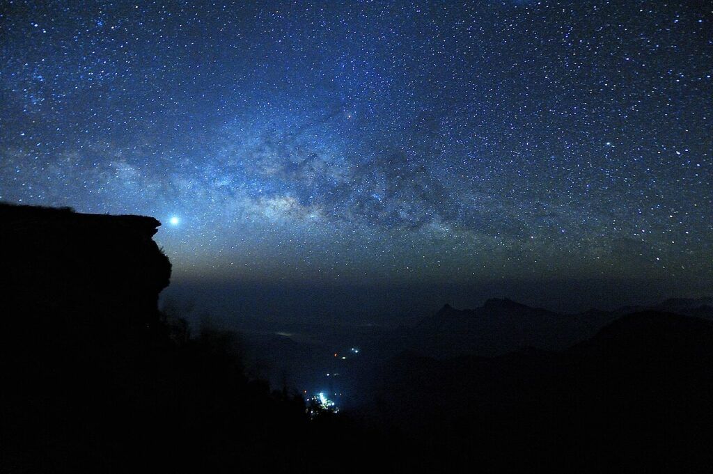 Milky Way over Phu Chi Fa’s cliff silhouette at night, with stars shining above the mountains in Chiang Rai, Thailand.