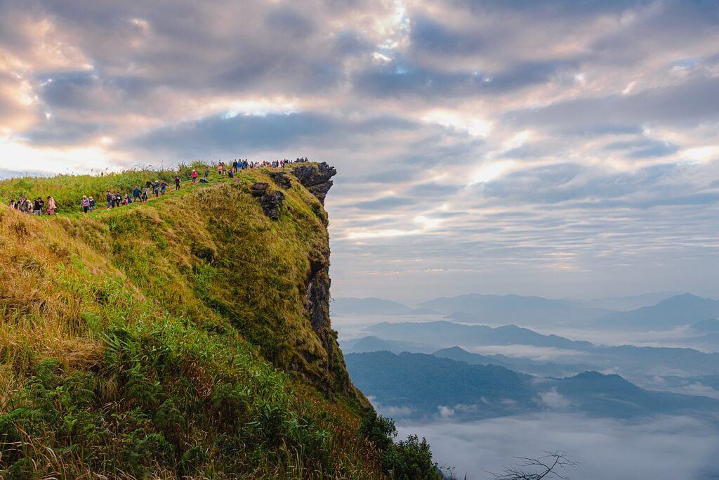 Crowds gathered along the ridge at Phu Chi Fa during a cloudy sunrise, overlooking mist-filled valleys in Chiang Rai, Thailand