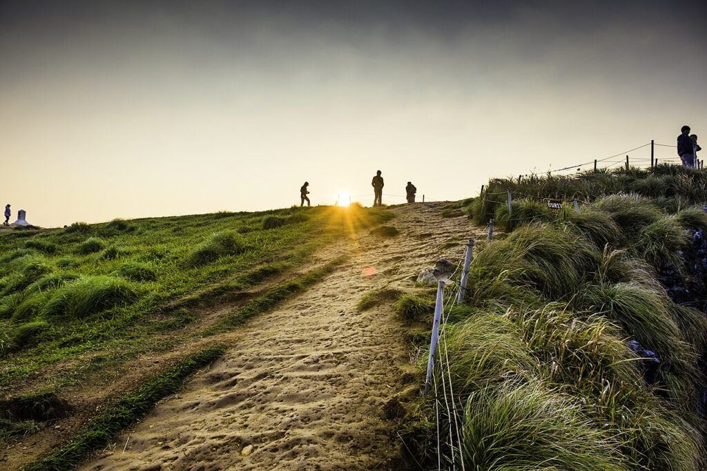 Hikers walking up the Phu Chi Fa sunrise trail in Chiang Rai, Thailand, with golden morning light on the ridge.