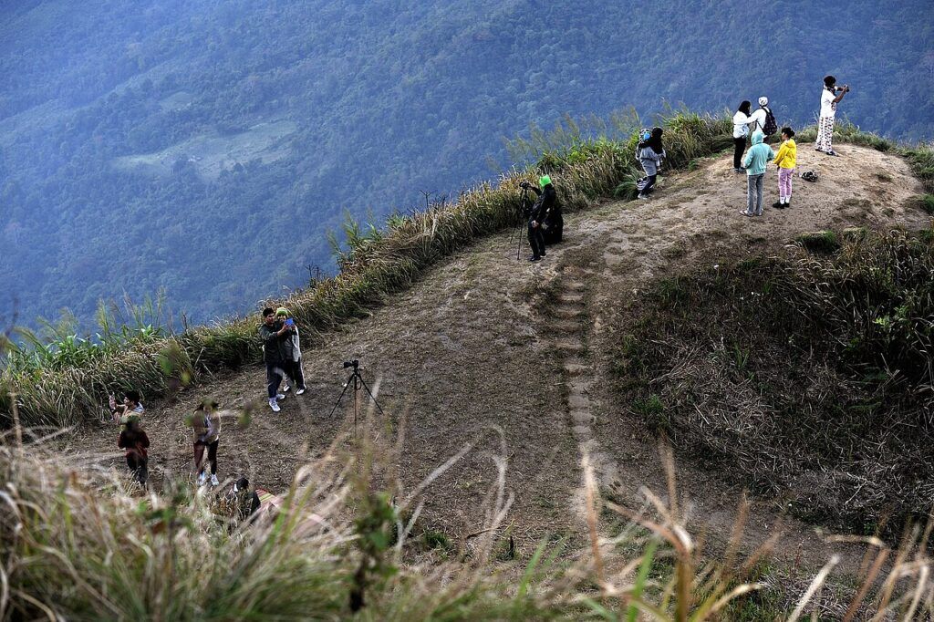 Visitors standing at the viewpoint area at Phu Chi Fa, Thailand, with mountain scenery in the background